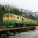 A vintage train rolls along the tracks over a shallow lake in the mountains